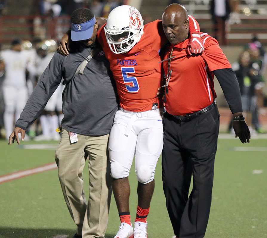 Panther Head Coach Reginald Samples assist trainer Alec Hawkins with giving starting quarterback Jaylin Nelson some support off the field after his season ending injury. (Jose Sanchez photo)